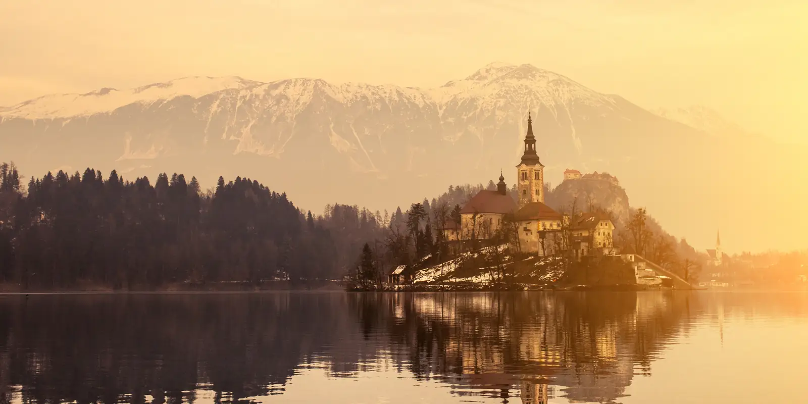 A church on a small island reflected in a still lake at golden hour