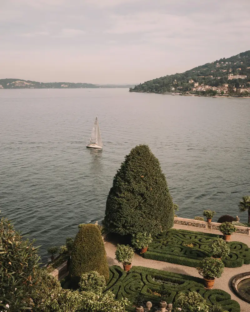 A lone sailboat on a lake beside a manicured garden